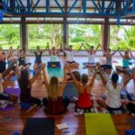 Yoga students sitting in a circle holding raised hands in Blue Osa's yoga shala in Costa Rica.