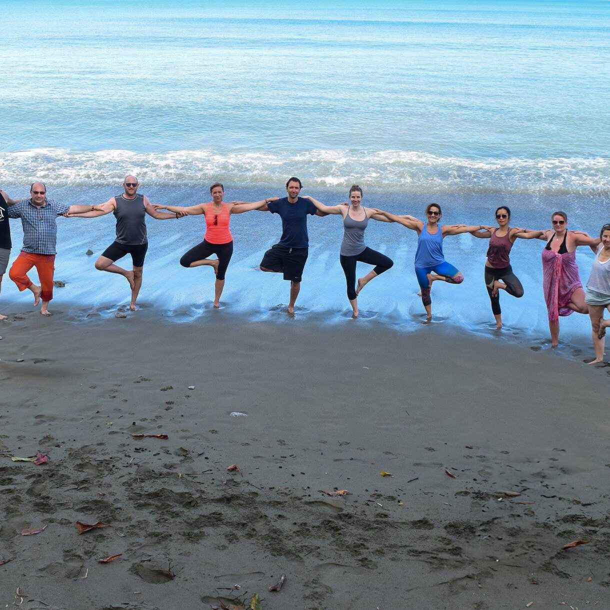 Group of yogis doing tree pose on the beach together facing the ocean during Blue Osa Yoga Retreat & Spa's Yoga Teacher Training Program in Costa Rica